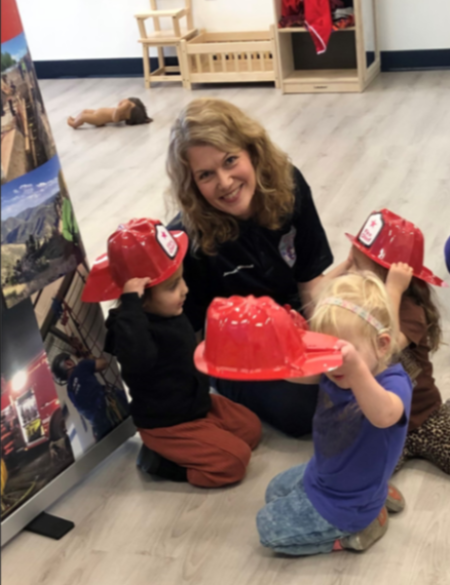 Image of woman sitting on the floor surrounded by children in a classroom