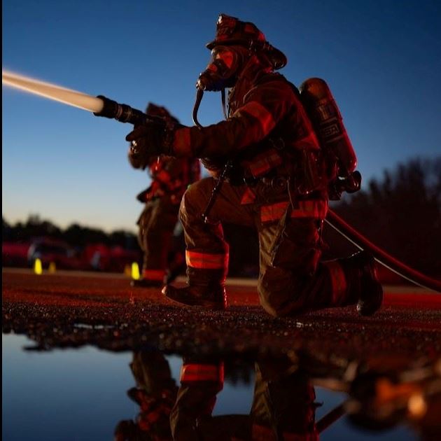 Firefighter kneeling, holding hose, and spraying water